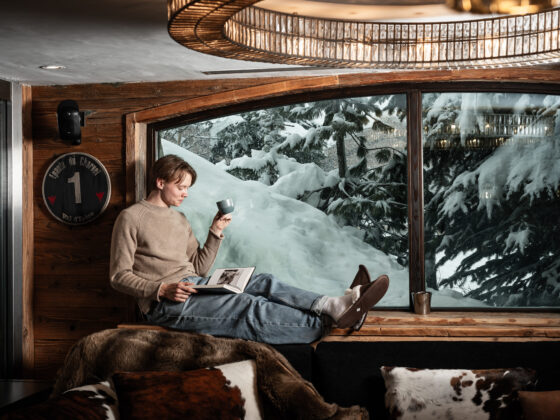 Young boy reading a book with coffee and mountain views at Chalet Lhotse, Val d’Isère, French Alps.